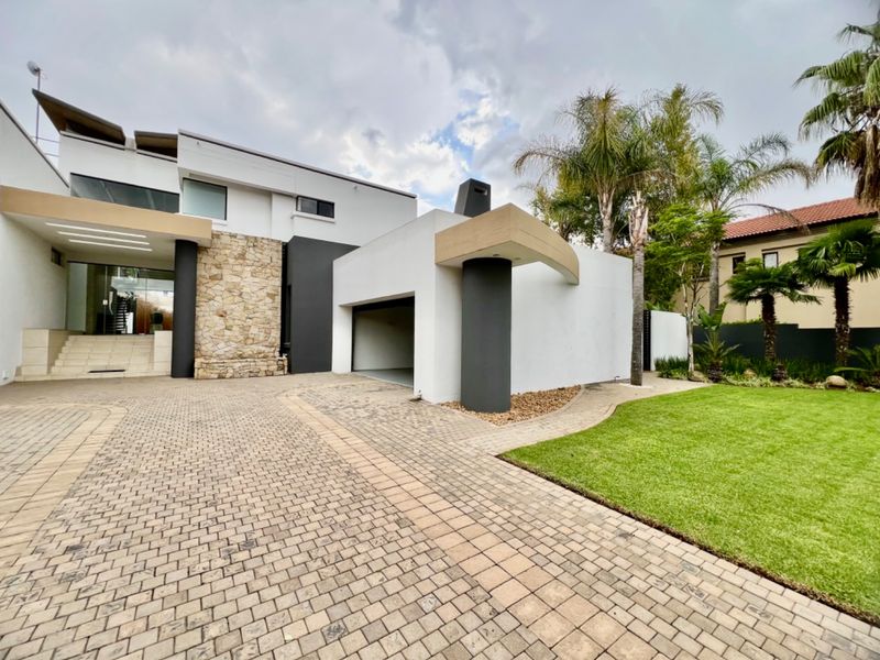 Modern architectural front facade featuring stone cladding, a paved driveway, and a well-maintained garden with a prominent garage entrance.