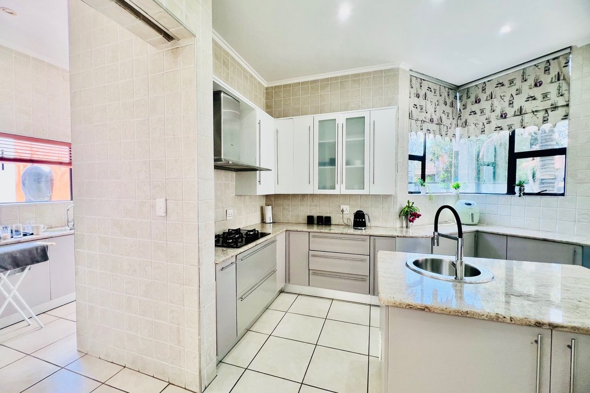 Modern kitchen featuring granite countertops, ample built-in cabinetry, a gas hob with extractor fan, and a convenient adjoining scullery area.