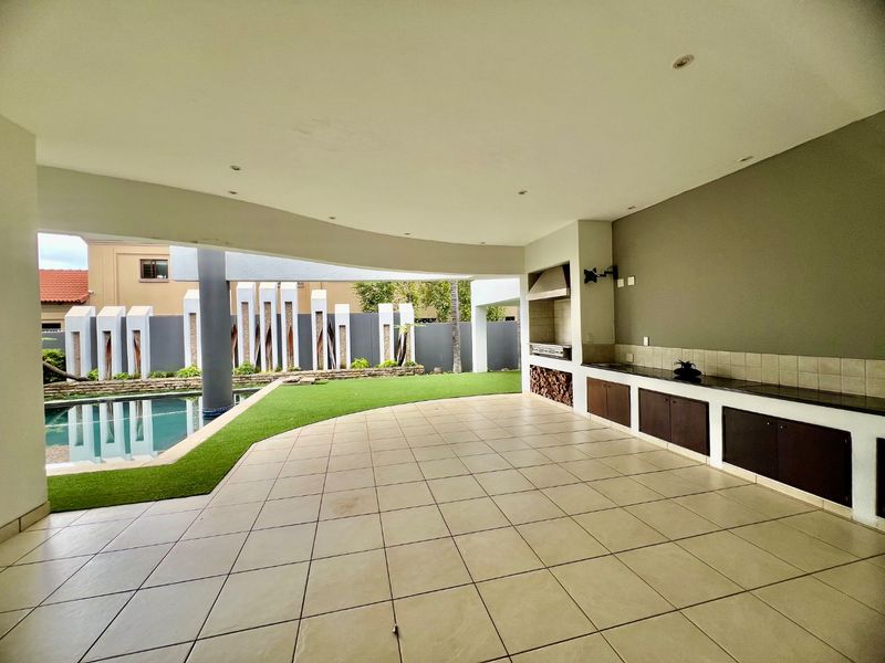 Spacious covered patio featuring a built-in braai, granite-topped cabinetry, and direct access to the swimming pool and landscaped garden area.