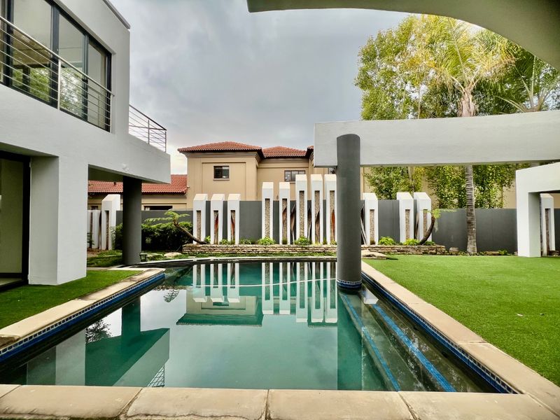 A modern outdoor pool area featuring a swimming pool, artificial lawn, and contemporary architectural boundary wall design.