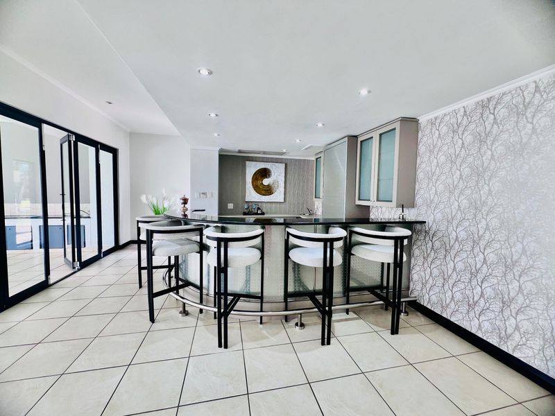A modern, well-maintained built-in bar area featuring a curved counter, glass-fronted cabinetry, recessed lighting, and tiled flooring with access to the patio.