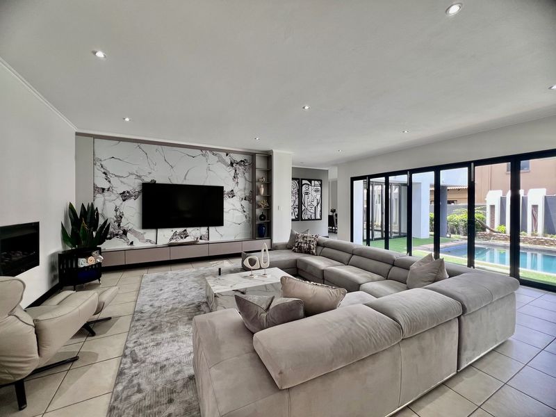 Spacious modern living room featuring a marble-look feature wall, built-in cabinetry, fireplace, and large bi-fold doors opening to the pool area.