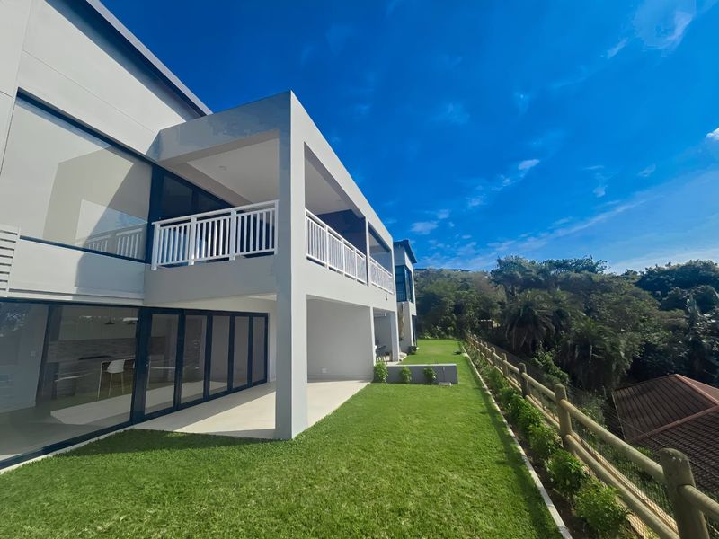 Rear view of a modern townhouse featuring a covered patio, upper balcony with railings, large sliding glass doors, and a well-maintained lawn.