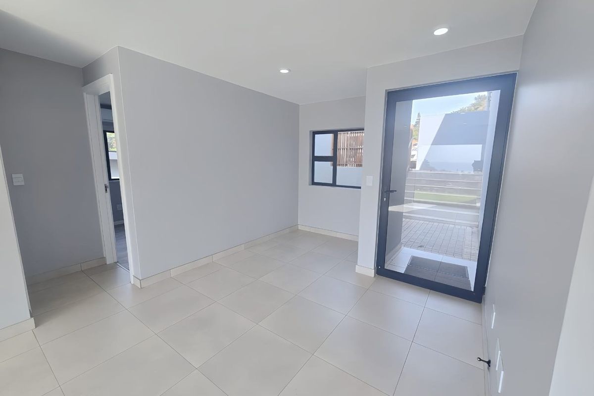 A bright, modern, and empty living area featuring neutral tiled flooring, recessed downlights, and direct access to an outdoor patio through a glass door.