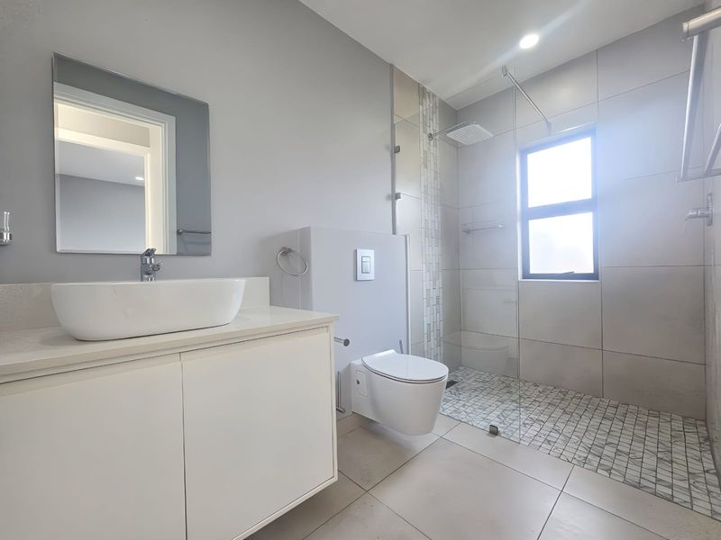 Modern bathroom featuring a wall-mounted vanity with vessel sink, wall-hung toilet, and a spacious walk-in shower with mosaic tile detailing.