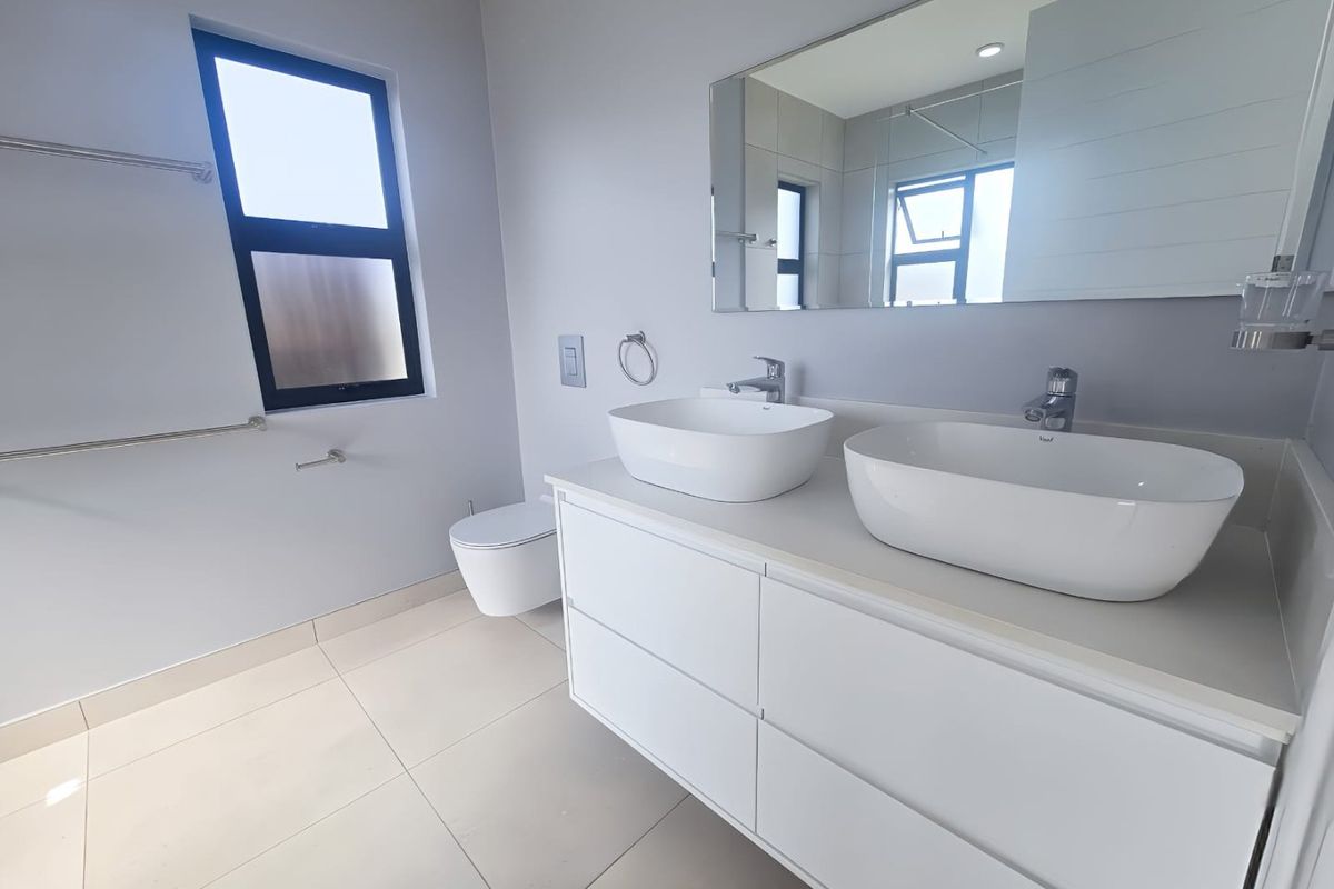 Modern bathroom featuring a sleek double vanity with vessel sinks, wall-mounted toilet, large mirror, and neutral floor tiling.