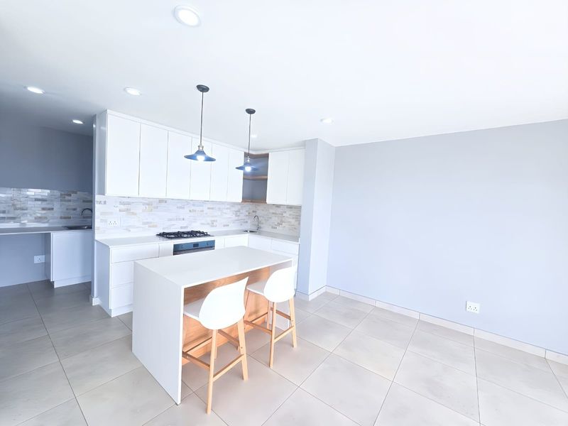 Modern open-plan kitchen featuring white cabinetry, stone countertops, a gas hob, and a central island, seamlessly integrated with a spacious living area.