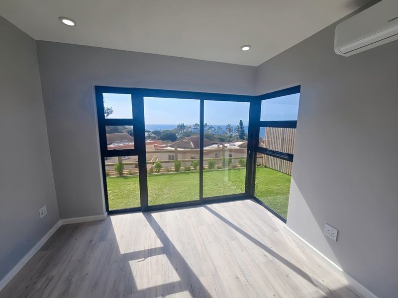 Bright and modern living area featuring light laminate flooring, recessed lighting, air conditioning, and large sliding doors opening to a garden with ocean views.
