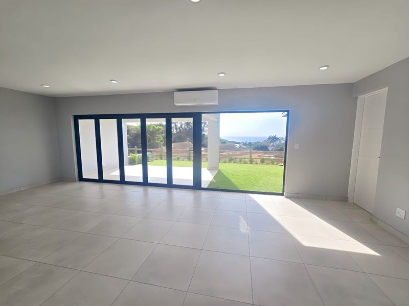 Spacious, modern living area featuring large aluminium stacker doors that open to a garden view, tiled floors, and integrated air conditioning.