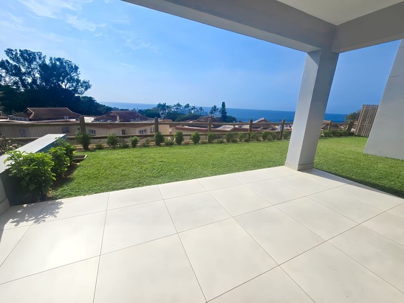 A spacious covered patio with large format floor tiles, overlooking a private lawn and offering scenic coastal views.