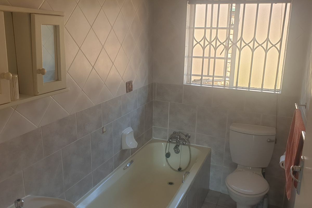 A functional bathroom featuring a bathtub, toilet, and wall-mounted medicine cabinet, finished with tiled walls and a security-gated window.