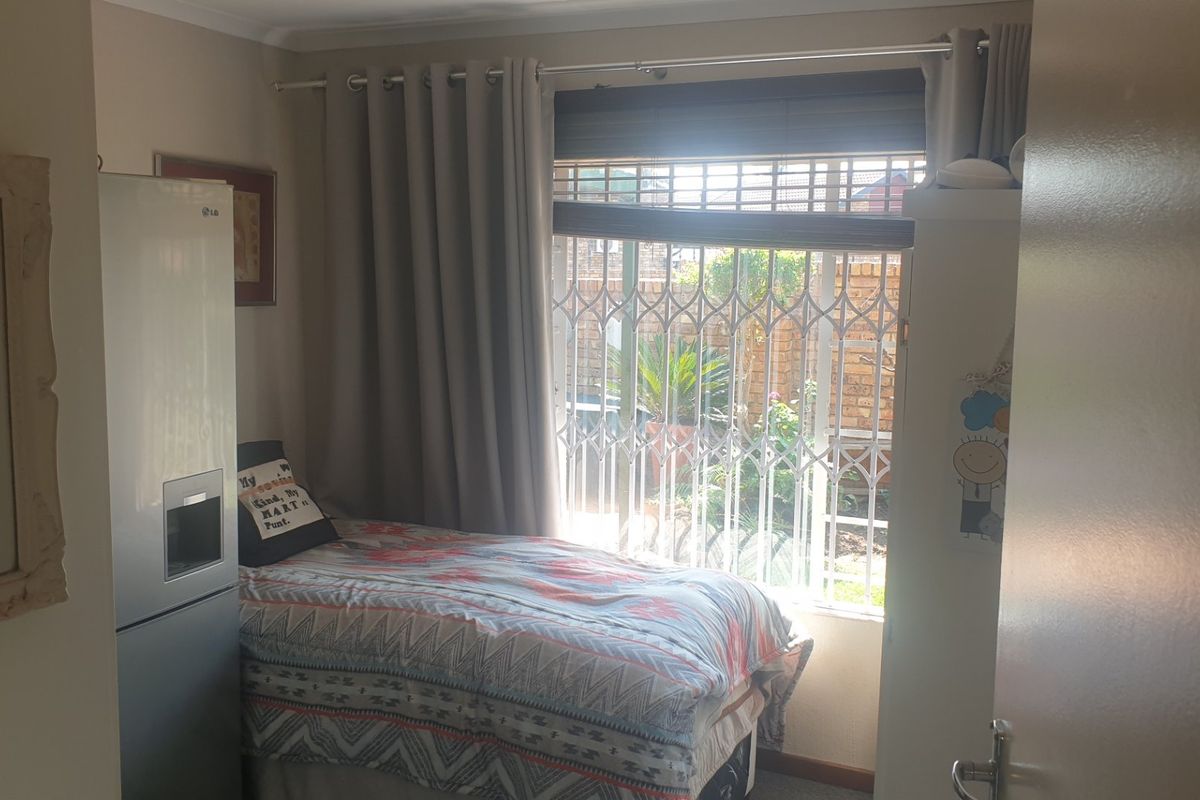 A compact bedroom featuring a window with a fitted security gate and neutral wall finishes.