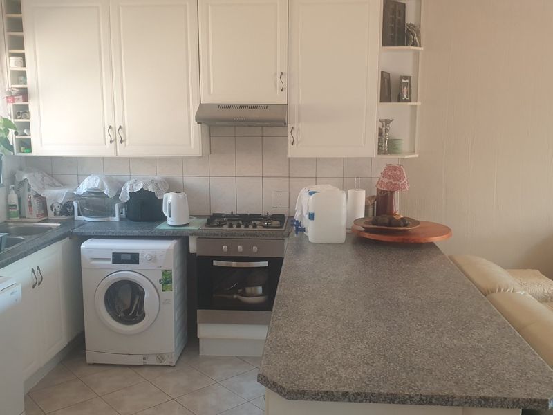 Open-plan kitchen featuring white cabinetry, laminate countertops, gas hob, built-in oven, and integrated laundry space, seamlessly connecting to the living area.