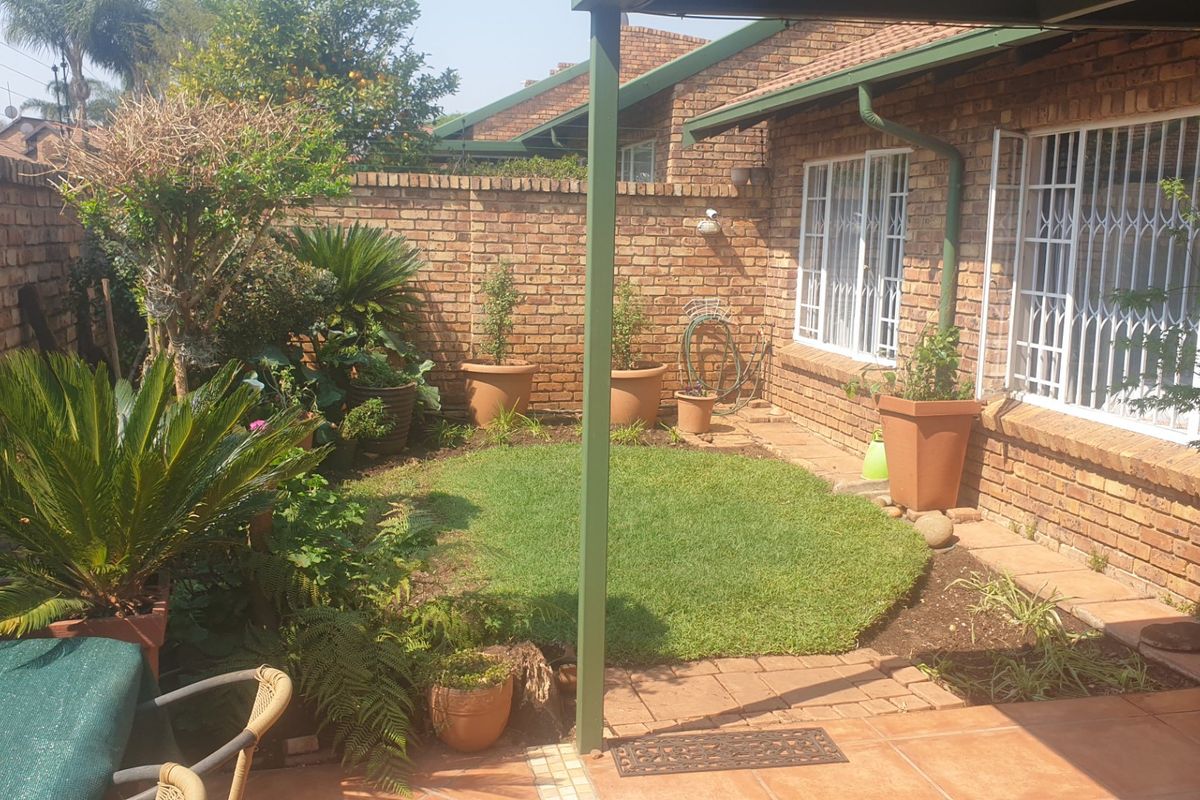 A private rear garden featuring a small lawn, brick boundary walls, and a covered tiled patio area with security bars on the windows.