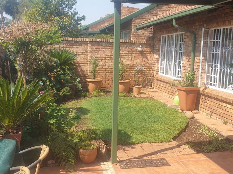 A private rear garden featuring a small lawn, brick boundary walls, and a covered tiled patio area with security bars on the windows.