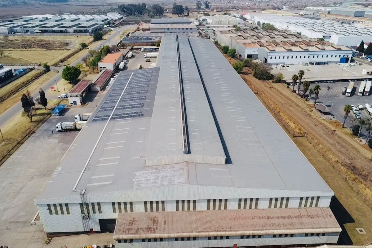Aerial view of a large industrial warehouse facility featuring a metal roof with solar panel installation and surrounding paved yard space.