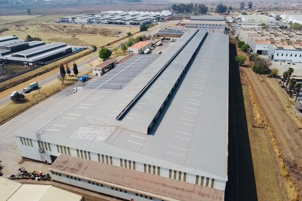 Aerial view of a large industrial warehouse facility featuring a metal roof with integrated solar panels and skylights in an established industrial park.