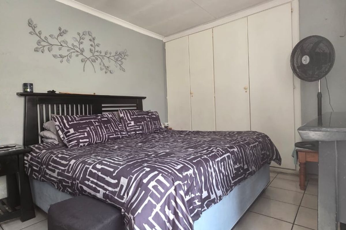 A bedroom featuring built-in cupboards and tiled flooring, requiring minor cosmetic updates to the wall finishes.