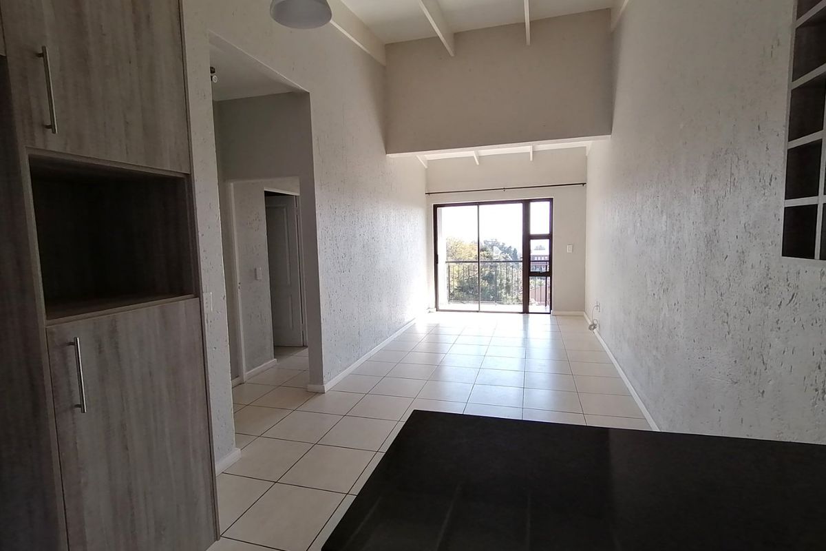 Spacious open-plan living area featuring tiled floors, high exposed beam ceilings, and direct access to a balcony through large sliding glass doors.