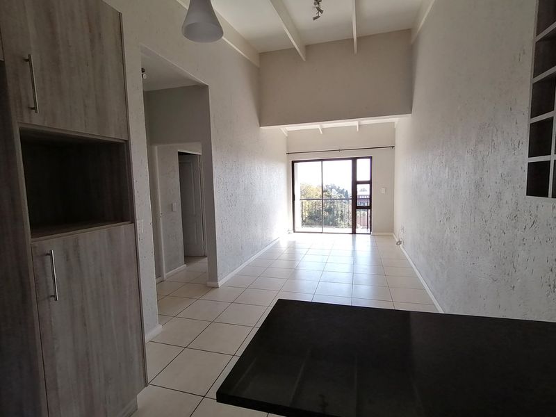 Spacious open-plan living area featuring tiled floors, high exposed beam ceilings, and direct access to a balcony through large sliding glass doors.