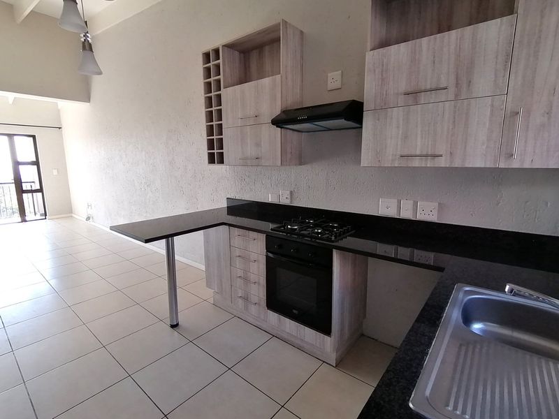 Modern open-plan kitchen featuring light wood-grain cabinetry, granite countertops, built-in gas hob, oven, and extractor fan, with tiled flooring throughout.