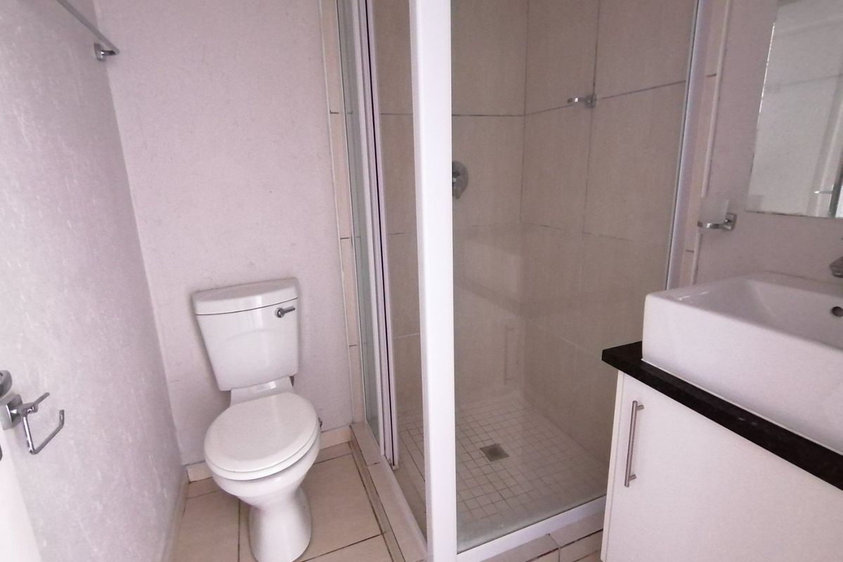 A functional bathroom featuring a shower enclosure, a white vanity cabinet with a basin, and a standard toilet, finished with neutral wall and floor tiles.