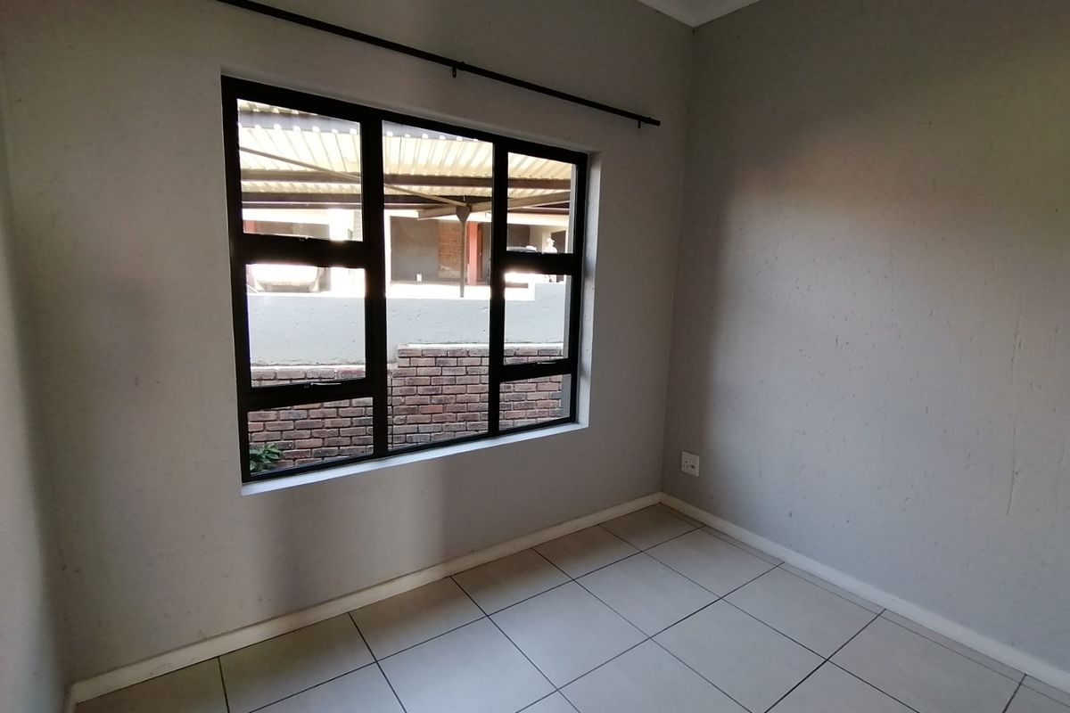 An empty bedroom featuring neutral tiled flooring, grey painted walls, and a black aluminium window frame overlooking the exterior area.