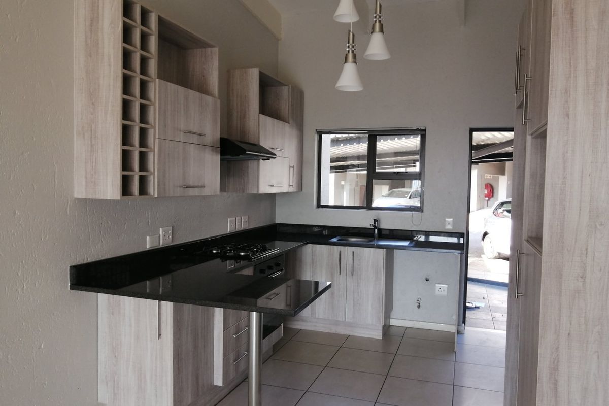 Modern kitchen featuring light wood-grain cabinetry, black granite countertops, a gas hob with extractor, and tiled flooring, offering a clean and functional workspace.