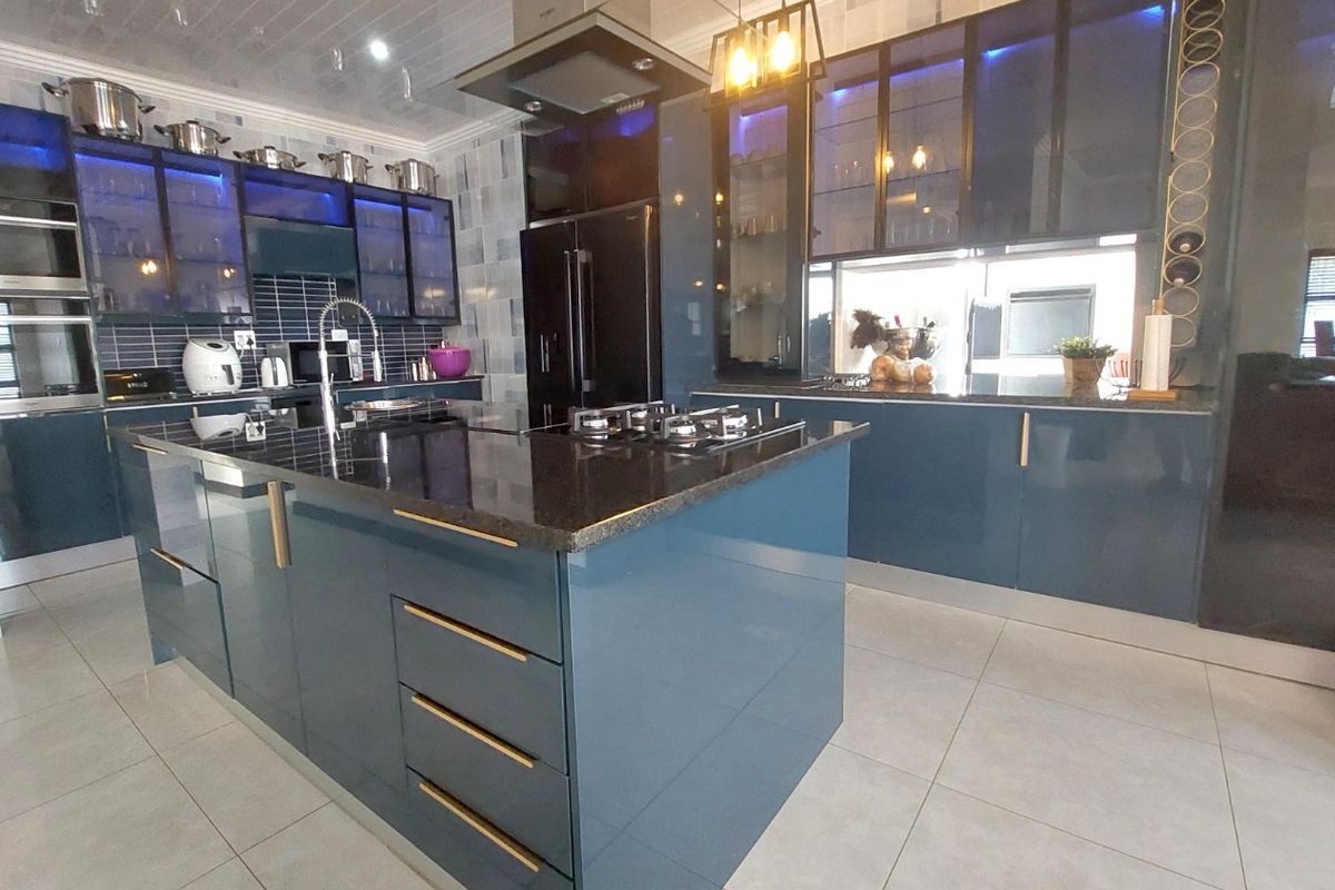 Modern kitchen featuring a large central island, granite countertops, gas cooktop, integrated extractor fan, and sleek blue cabinetry with ambient lighting.