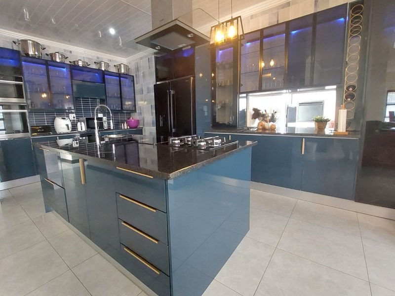 Modern kitchen featuring a large central island, granite countertops, gas cooktop, integrated extractor fan, and sleek blue cabinetry with ambient lighting.