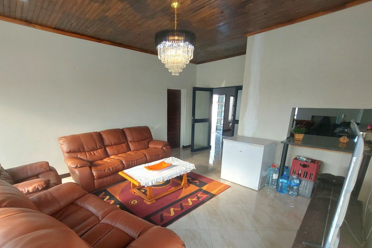 Spacious living room featuring a distinctive timber ceiling, tiled flooring, and a central crystal chandelier, offering a versatile layout for comfortable family living.