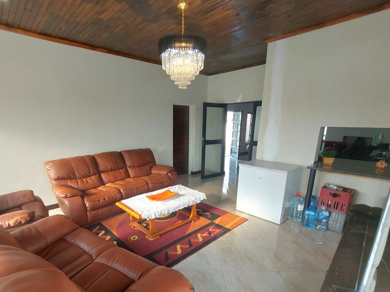 Spacious living room featuring a distinctive timber ceiling, tiled flooring, and a central crystal chandelier, offering a versatile layout for comfortable family living.