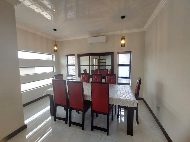 A well-maintained dining room featuring tiled flooring, coved ceilings, modern pendant lighting, and a wall-mounted split-system air conditioner.