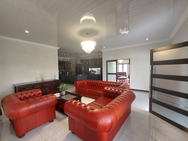 Spacious open-plan living area featuring glossy ceilings, recessed lighting, and tiled floors, seamlessly connecting to a modern kitchen with dark cabinetry.