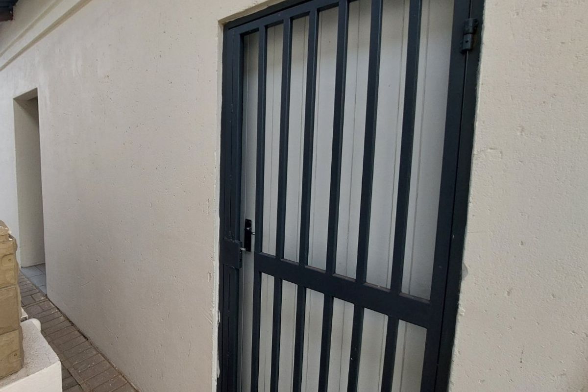 A side or rear exterior view showing a paved walkway and a black metal security gate installed on a plastered wall.