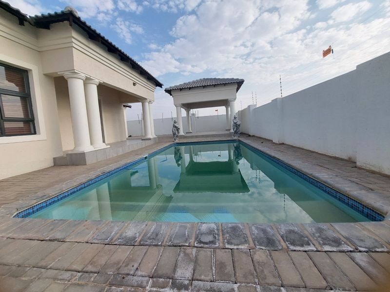 Outdoor pool area featuring a swimming pool, paved surround, and a covered gazebo structure with classical columns, enclosed by a perimeter wall.