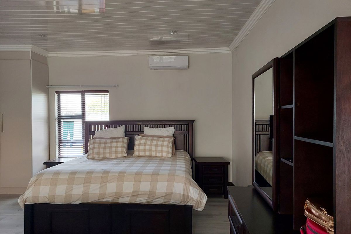 A well-maintained bedroom featuring laminate flooring, a split-system air conditioner, built-in cupboards, and venetian blinds.
