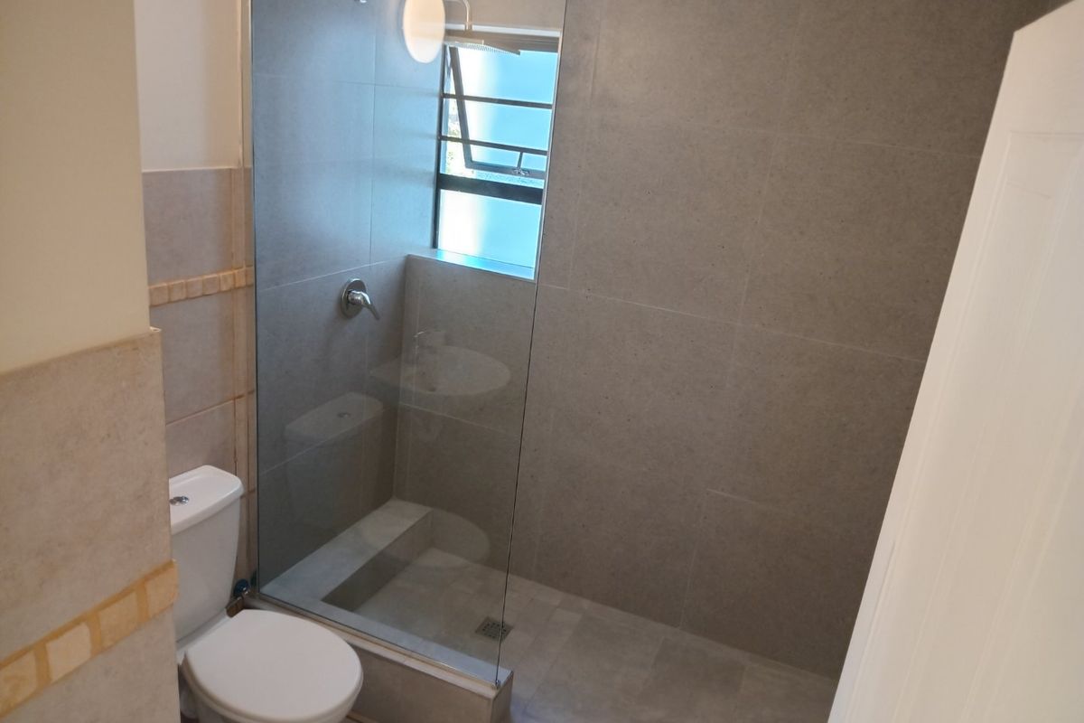 Modern bathroom featuring a walk-in shower with a glass screen, neutral wall and floor tiling, and a standard toilet.