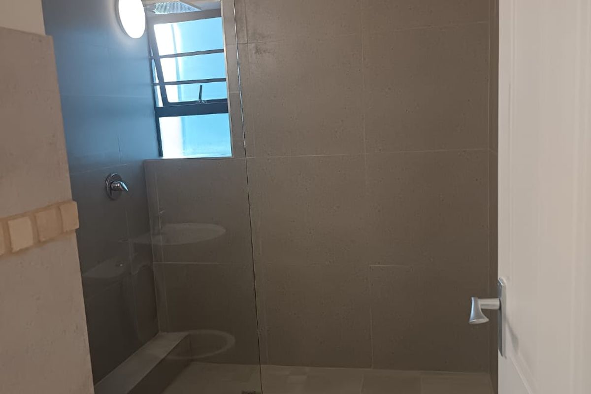 A modern bathroom featuring a walk-in shower with a glass screen, neutral wall and floor tiling, and a louver window for ventilation.