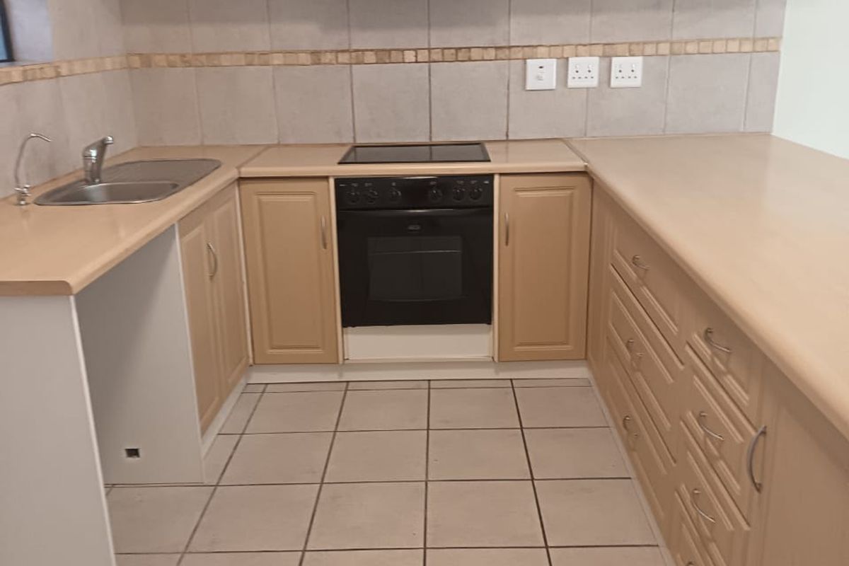 A functional kitchen featuring light wood-tone cabinetry, laminate countertops, built-in oven with hob, and neutral ceramic floor tiles.