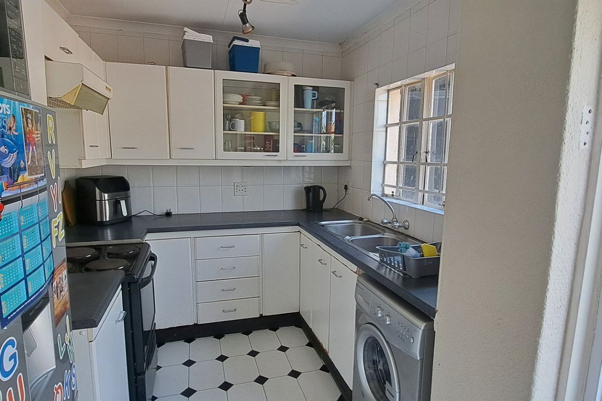 A functional kitchen featuring white built-in cabinetry, dark laminate countertops, a double bowl sink, and tiled flooring with a classic checkerboard pattern.