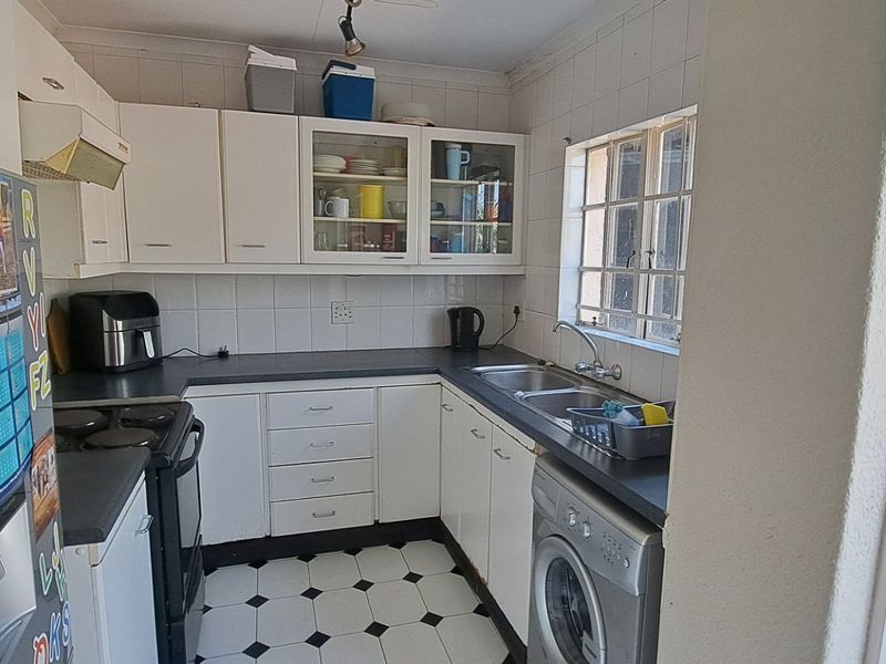A functional kitchen featuring white built-in cabinetry, dark laminate countertops, a double bowl sink, and tiled flooring with a classic checkerboard pattern.