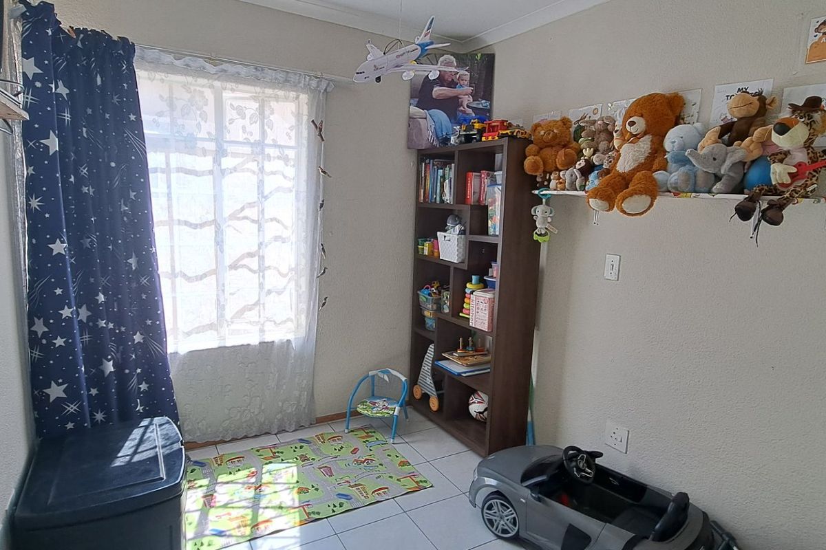 A functional bedroom featuring tiled flooring and a window, currently utilized as a children's play area.