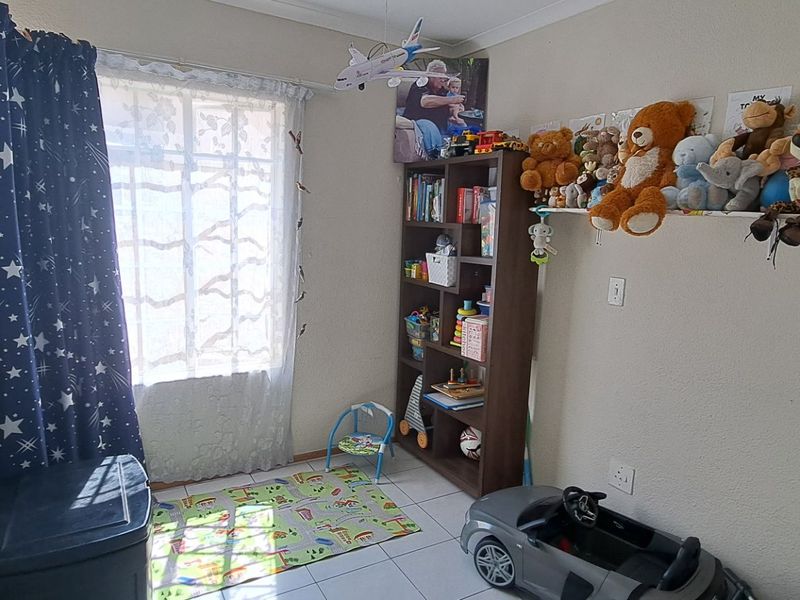 A functional bedroom featuring tiled flooring and a window, currently utilized as a children's play area.