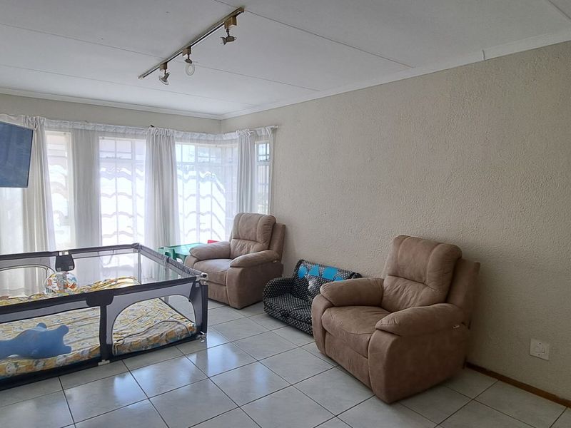 A living room featuring tiled flooring, track lighting, and large windows that provide natural light.