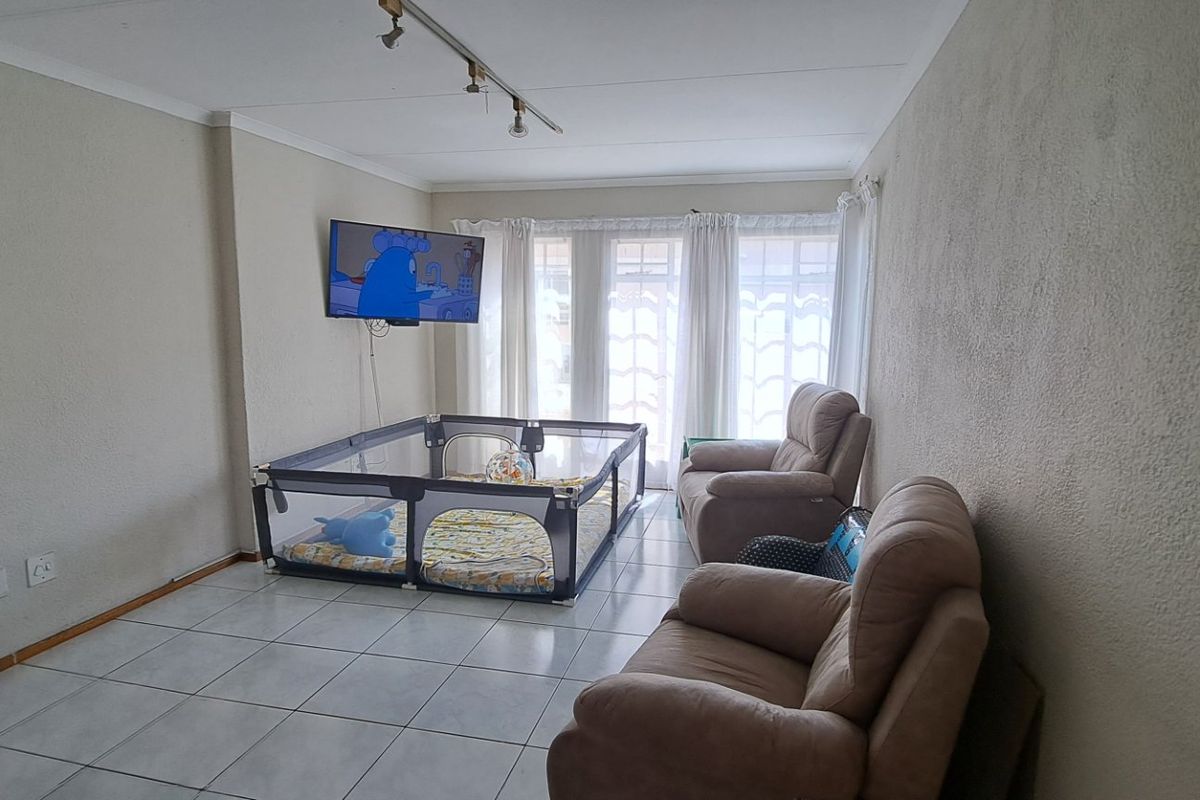 A living room featuring tiled flooring, track lighting, and a sliding glass door providing natural light.