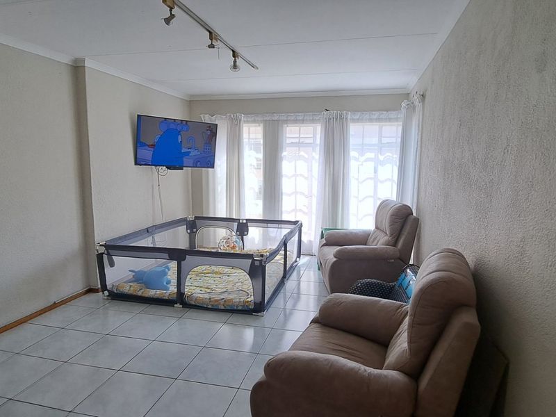 A living room featuring tiled flooring, track lighting, and a sliding glass door providing natural light.