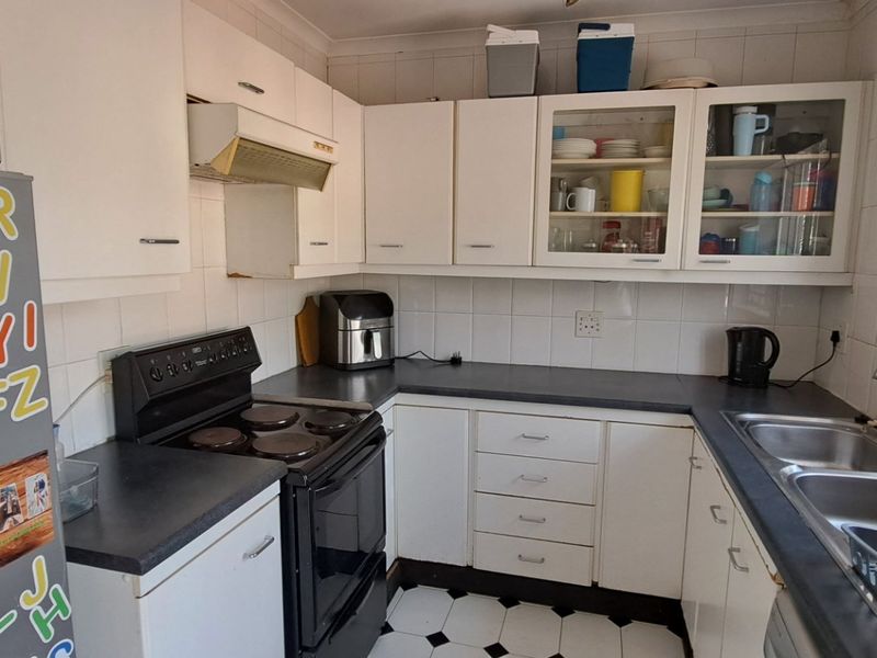 A functional kitchen featuring white built-in cabinetry, dark laminate countertops, a double basin sink, and a tiled backsplash with classic checkerboard floor tiles.