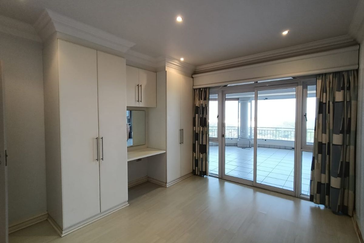 Spacious bedroom featuring built-in cupboards, an integrated vanity desk, recessed lighting, and sliding glass doors leading to a private balcony.