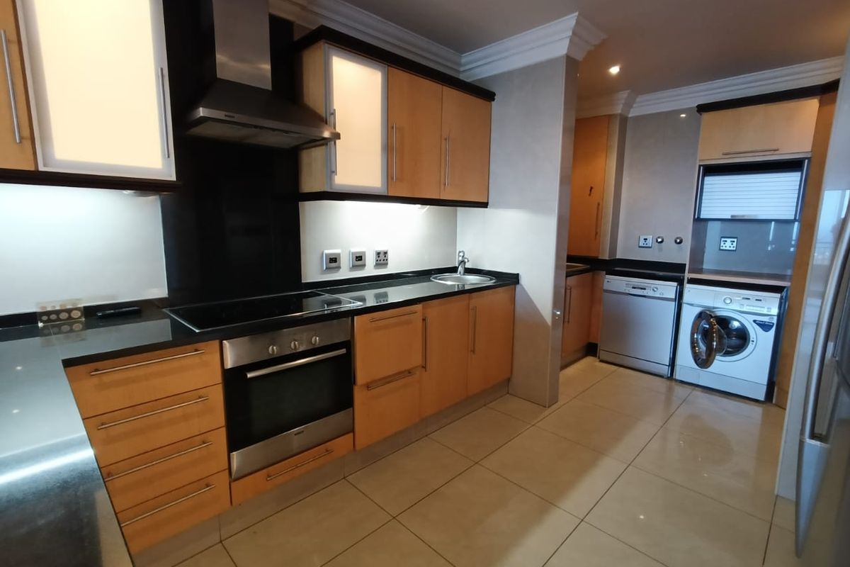 Modern kitchen featuring light wood cabinetry, dark stone countertops, integrated stainless steel appliances, and tiled flooring with a dedicated laundry area.